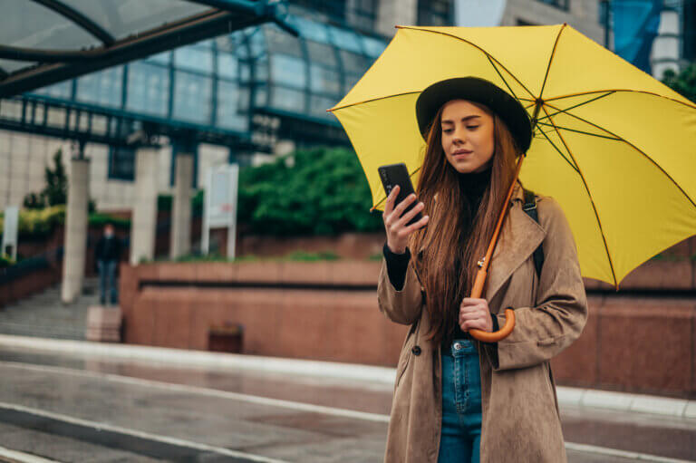 Advanced Weather Optimization product concept shown as a woman in a trench coat and black hat under a bright yellow umbrella in an urban setting