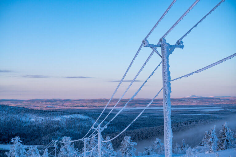 Power lines covered in frost against a winter landscape with snow-covered trees and mountains in the background.