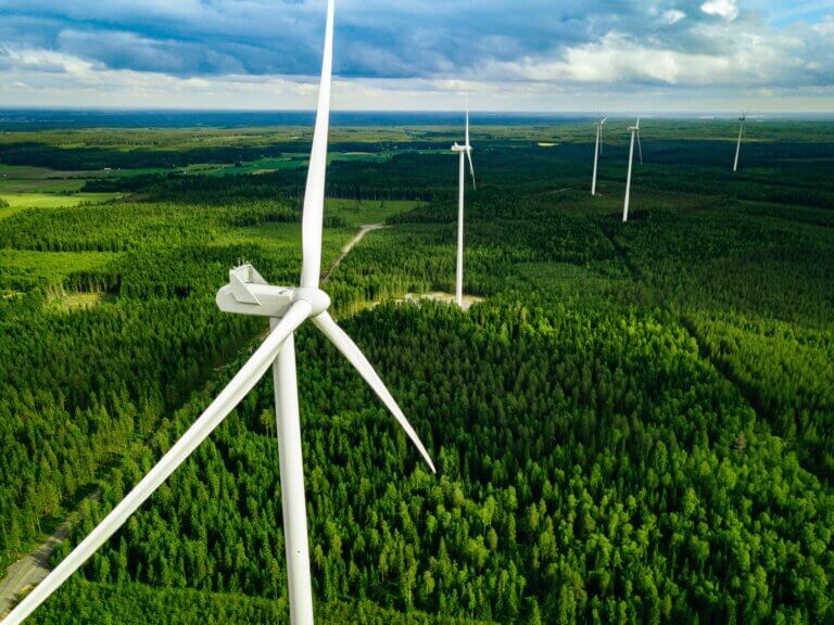 Aerial view of wind turbines situated in a green forested landscape with cloudy skies.