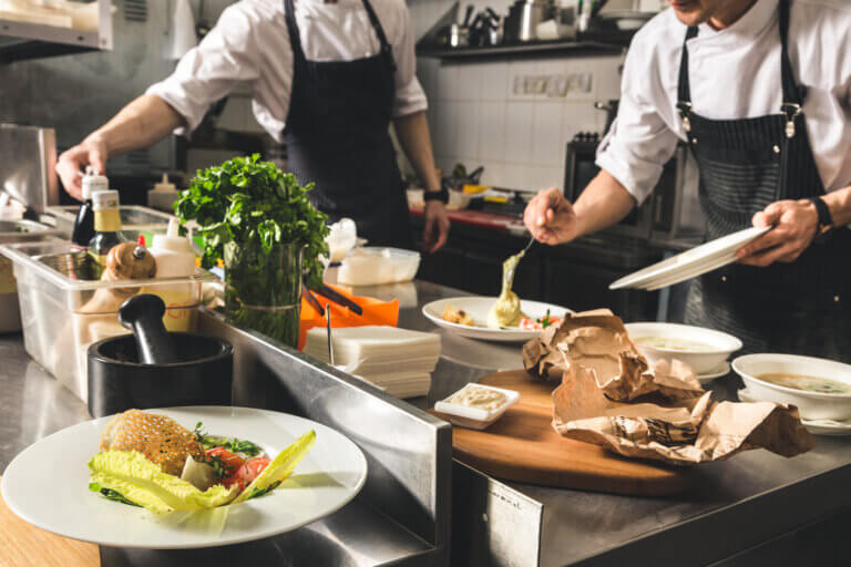 Two chefs working in a kitchen, one plating food while the other prepares ingredients.