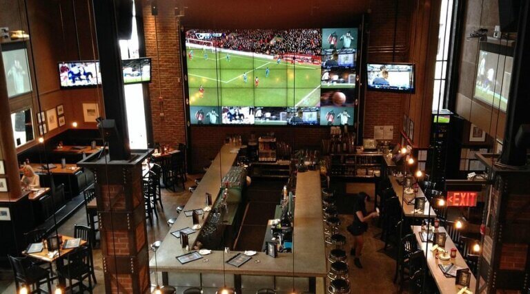 Interior of a restaurant featuring a bar area and multiple screens displaying sports events.