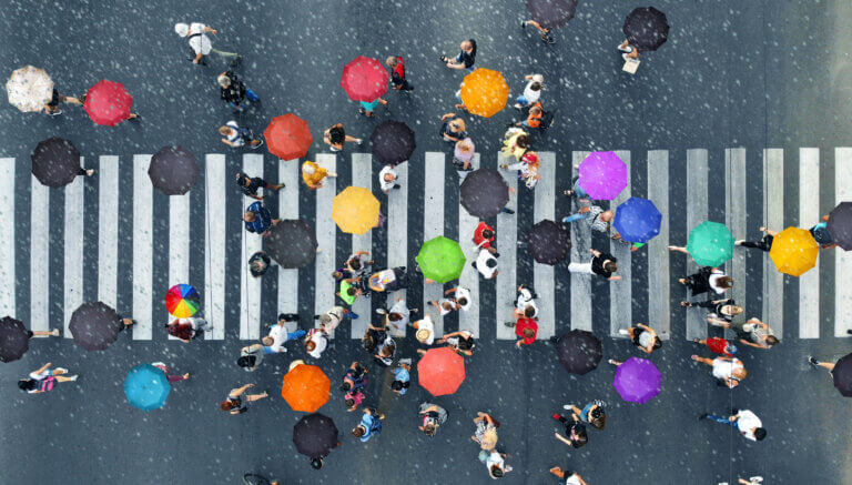 Aerial view of people with colorful umbrellas on a rainy street crosswalk.